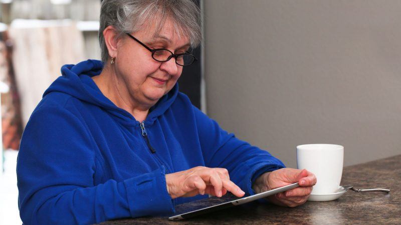 Elderly lady using tablet while drinking a hot beverage
